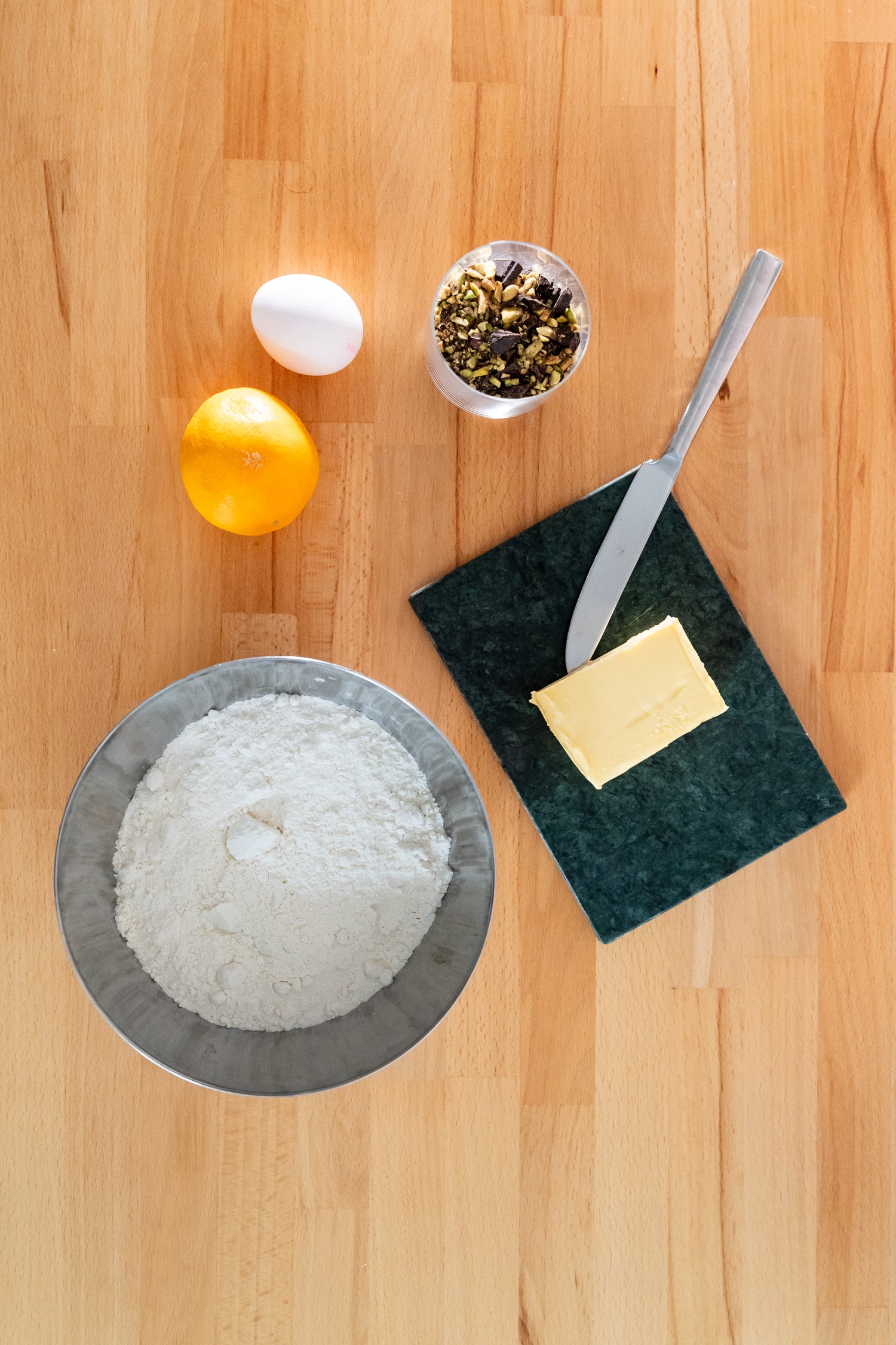 Baking ingredients including flour, butter, pistachios, chocolate, and orange