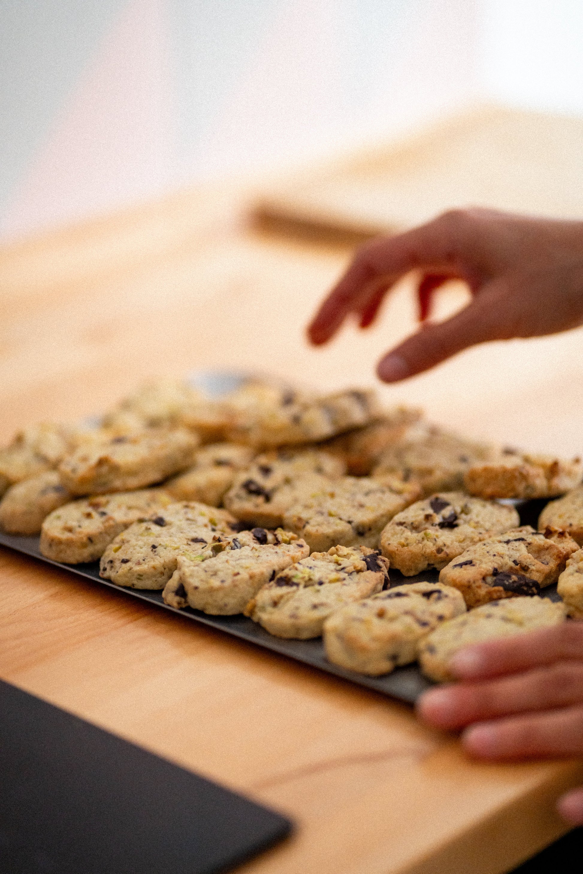 Hand reaching towards a tray of cookies on a wooden surface