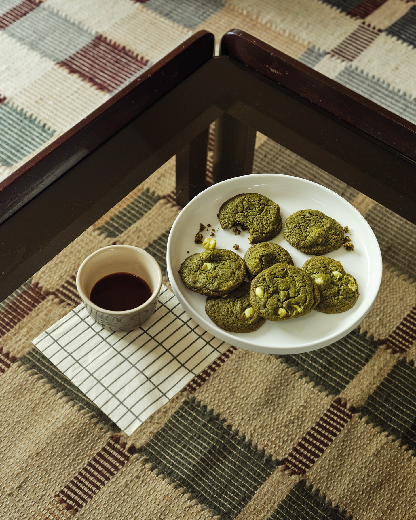 matcha cookies on a white plate with a cup of coffee on a checkered tablecloth.
