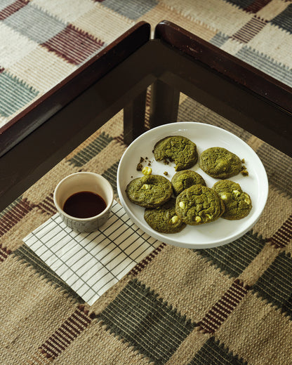 matcha cookies on a white plate with a cup of coffee on a checkered tablecloth.